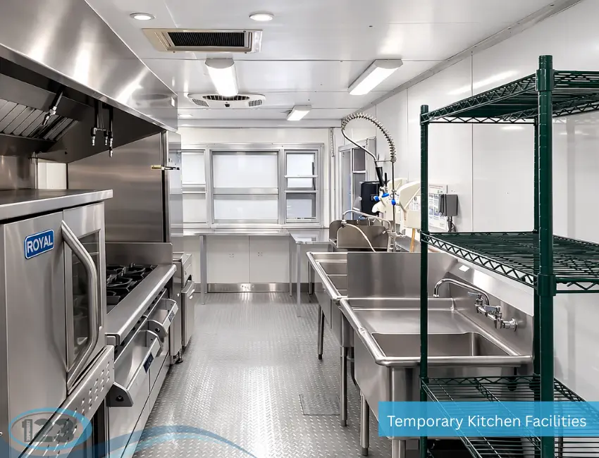 Clean mobile kitchen trailer interior with stainless steel sinks, commercial stove, ventilation hood, and storage shelving